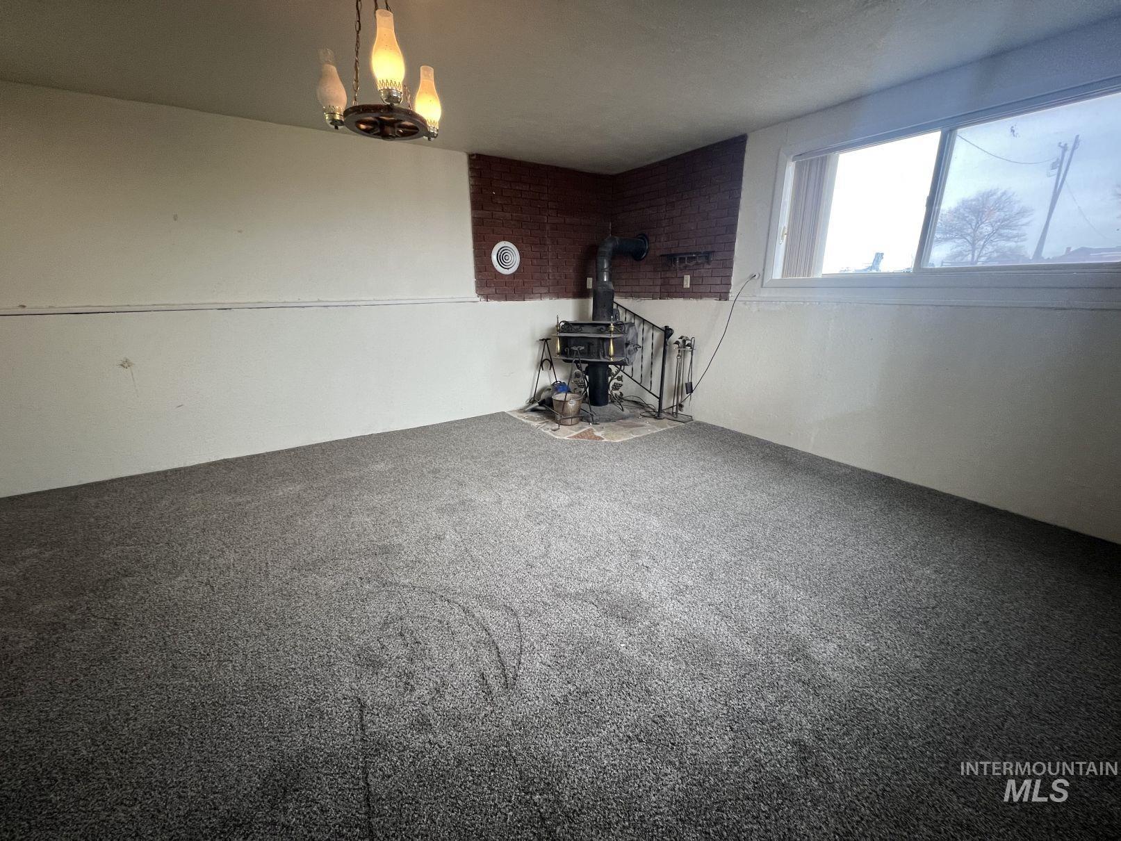 Unfurnished living room featuring a wood stove, carpet, and a chandelier