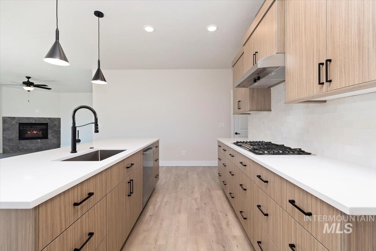Kitchen featuring hanging light fixtures, light wood-style flooring, backsplash, a premium fireplace, and light brown cabinets