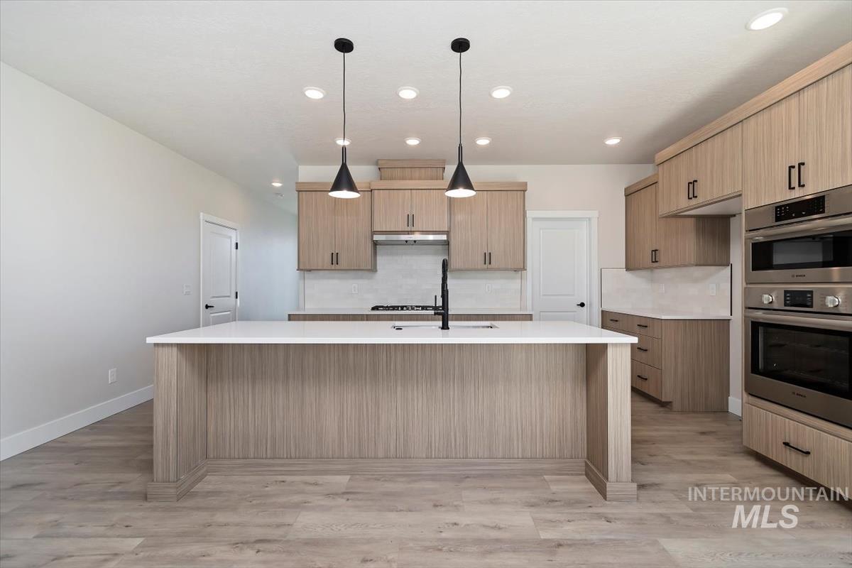 Kitchen featuring decorative backsplash, pendant lighting, double oven, an island with sink, and recessed lighting