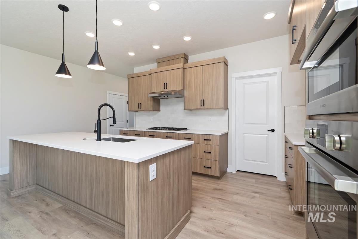 Kitchen featuring hanging light fixtures, decorative backsplash, appliances with stainless steel finishes, light wood-type flooring, and light stone counters
