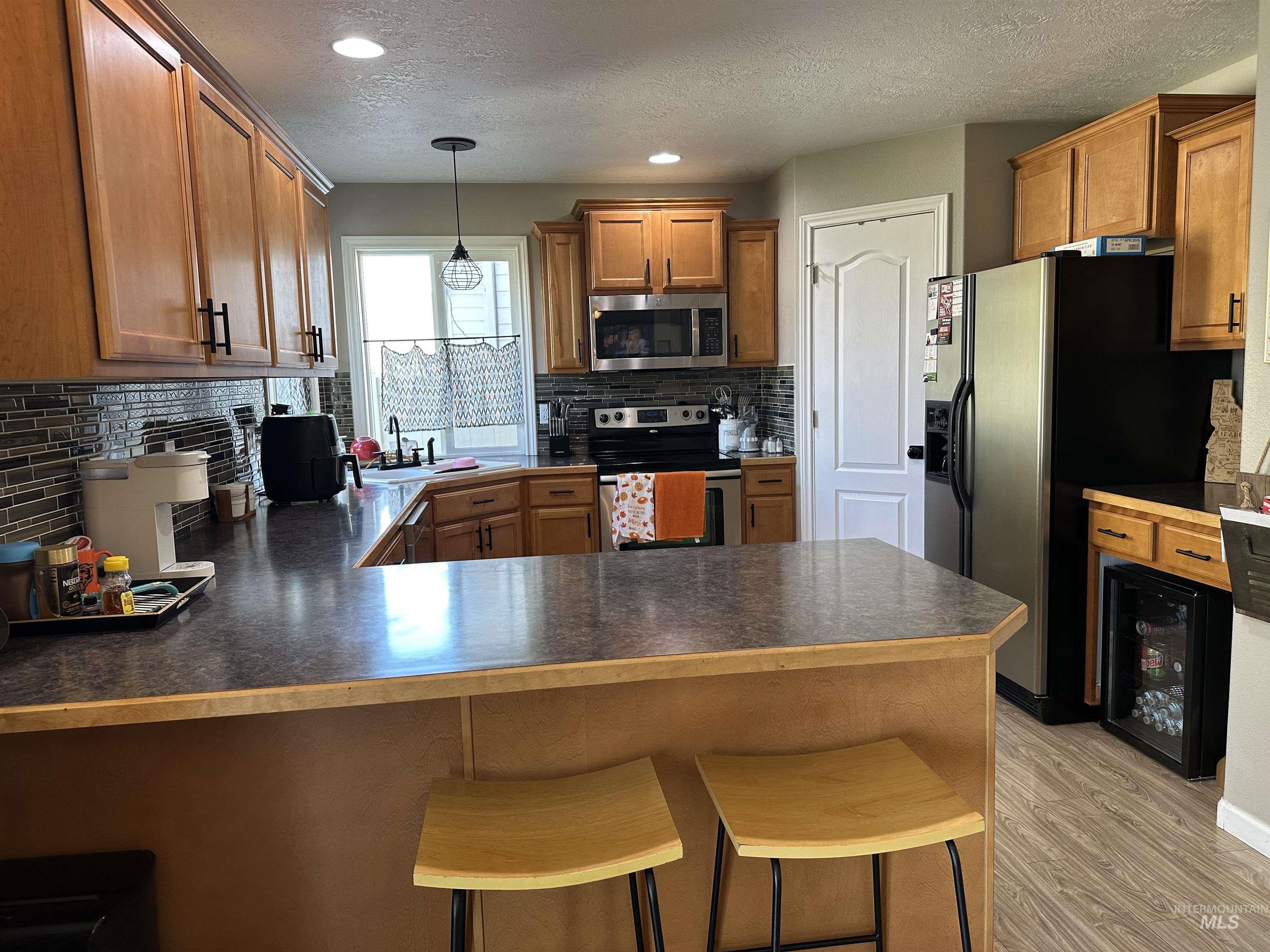 Kitchen with dark countertops, brown cabinets, stainless steel appliances, a textured ceiling, and hanging light fixtures