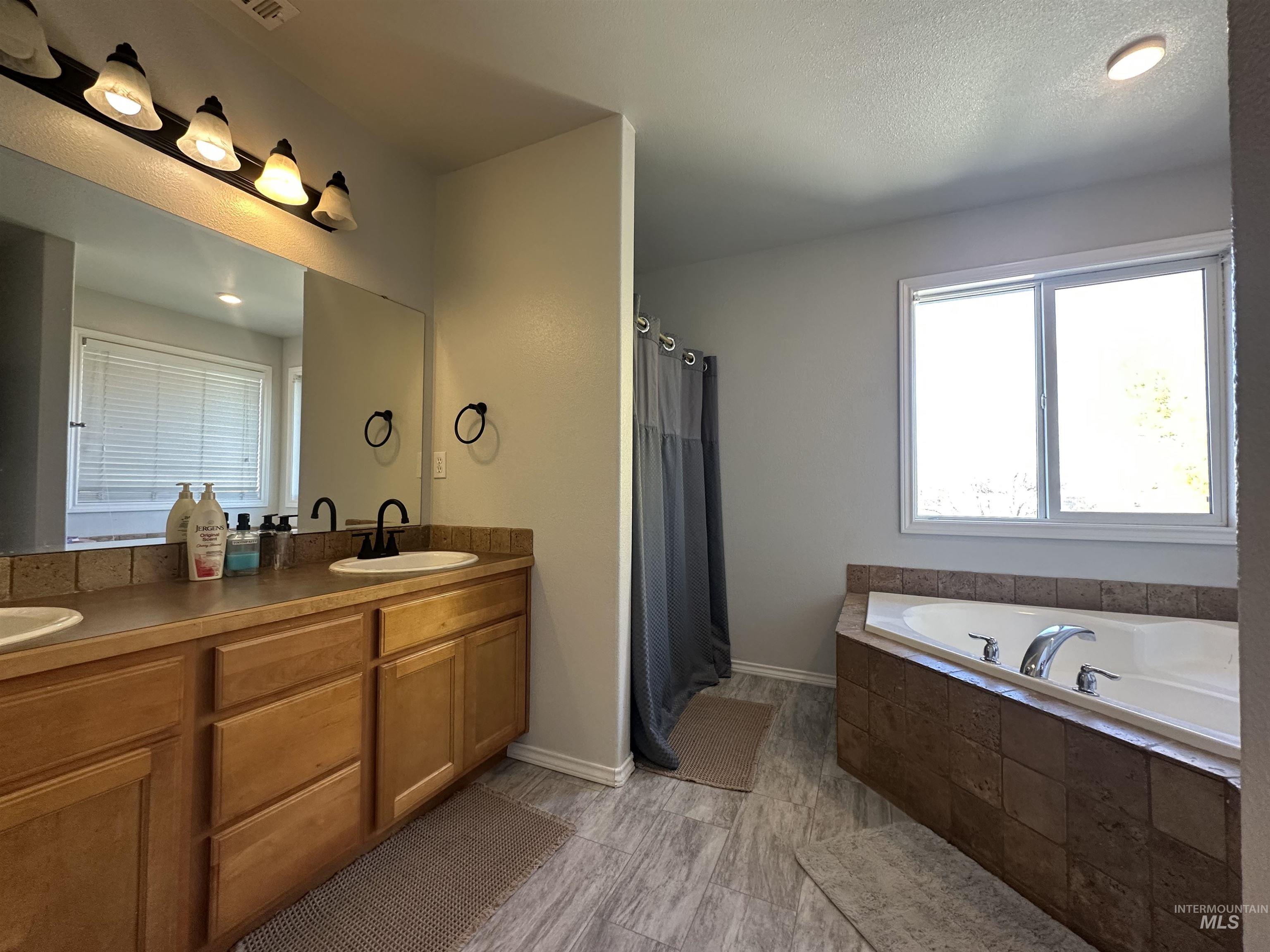 Bathroom with double vanity, a garden tub, a shower with shower curtain, and a textured ceiling