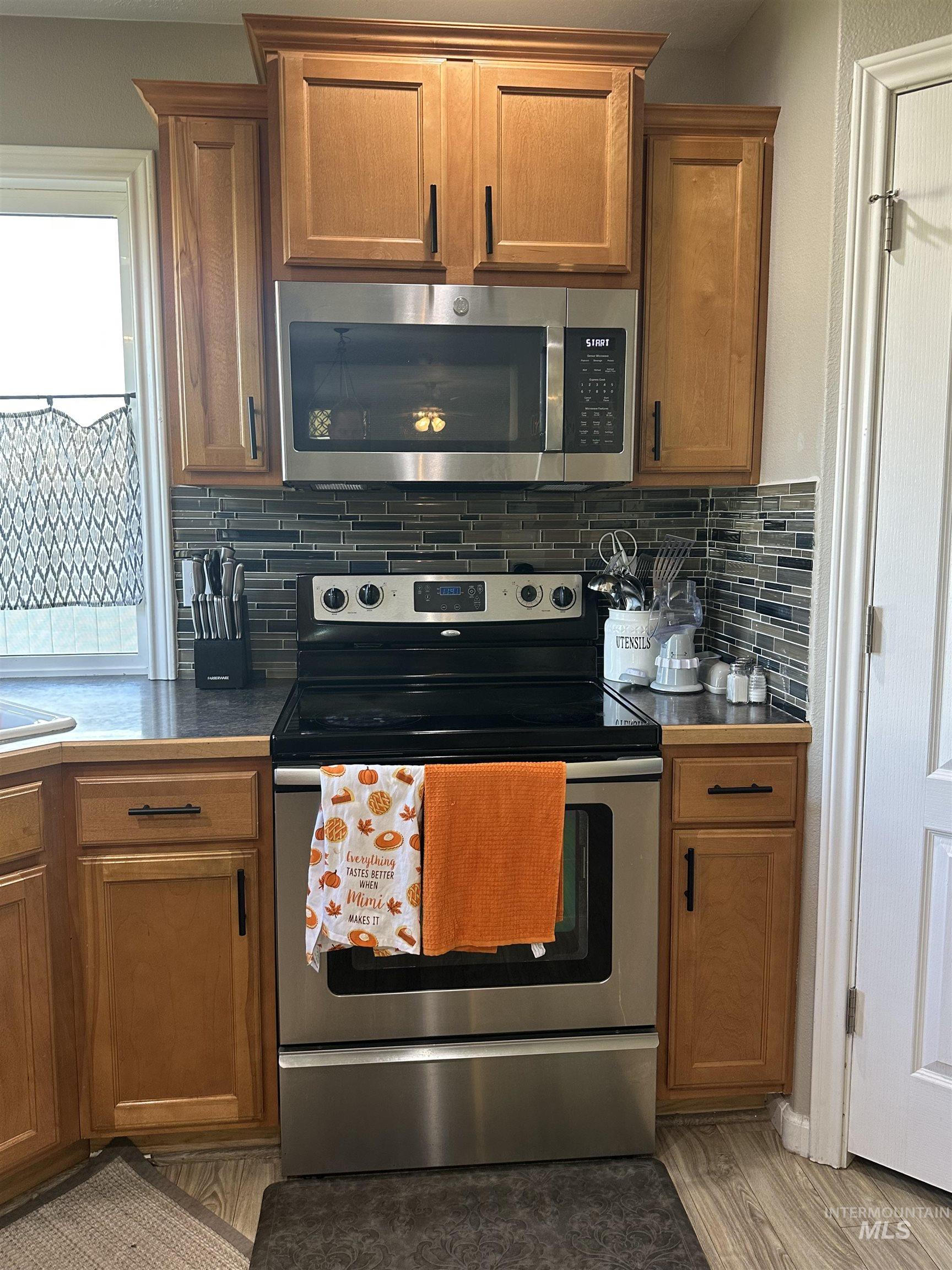 Kitchen with appliances with stainless steel finishes, brown cabinetry, backsplash, and light wood-style flooring
