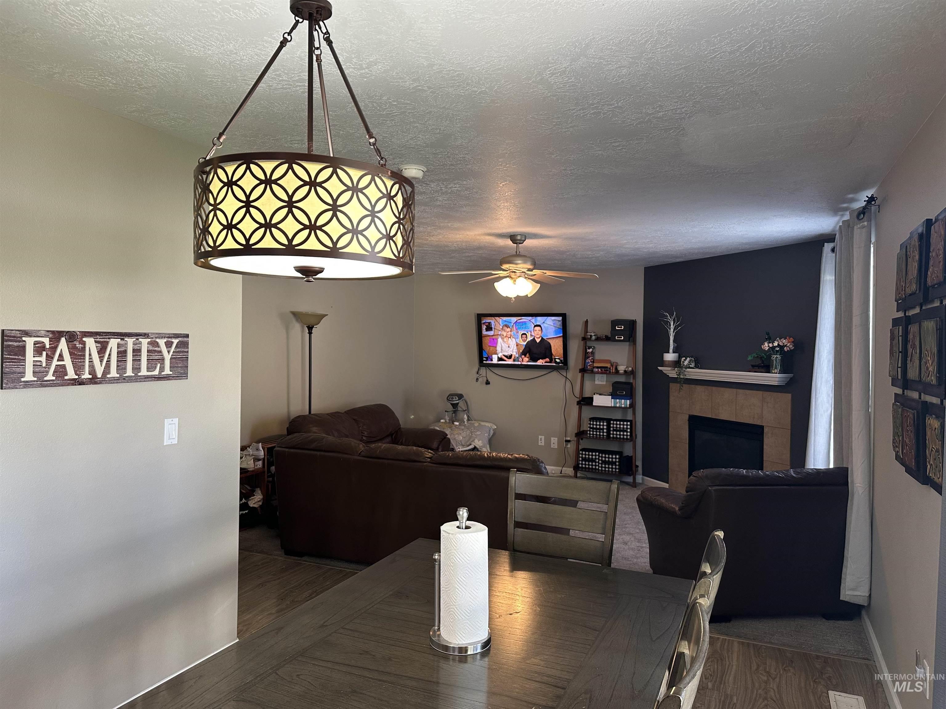 Dining area with wood finished floors, a textured ceiling, a fireplace, and ceiling fan