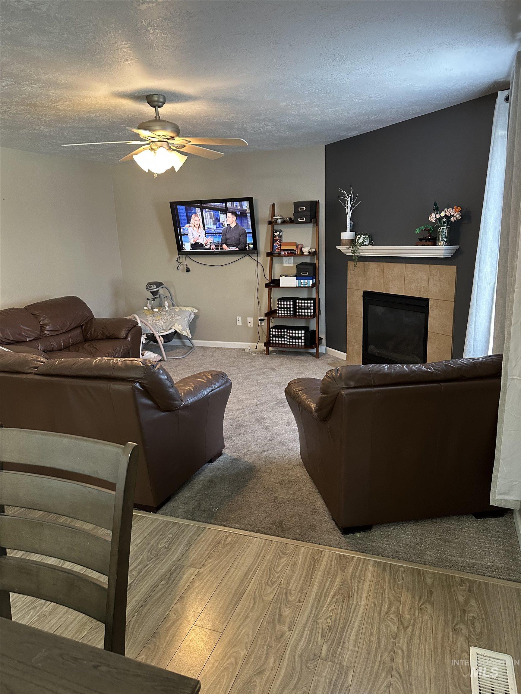 Living room featuring a textured ceiling, a tile fireplace, wood finished floors, and a ceiling fan