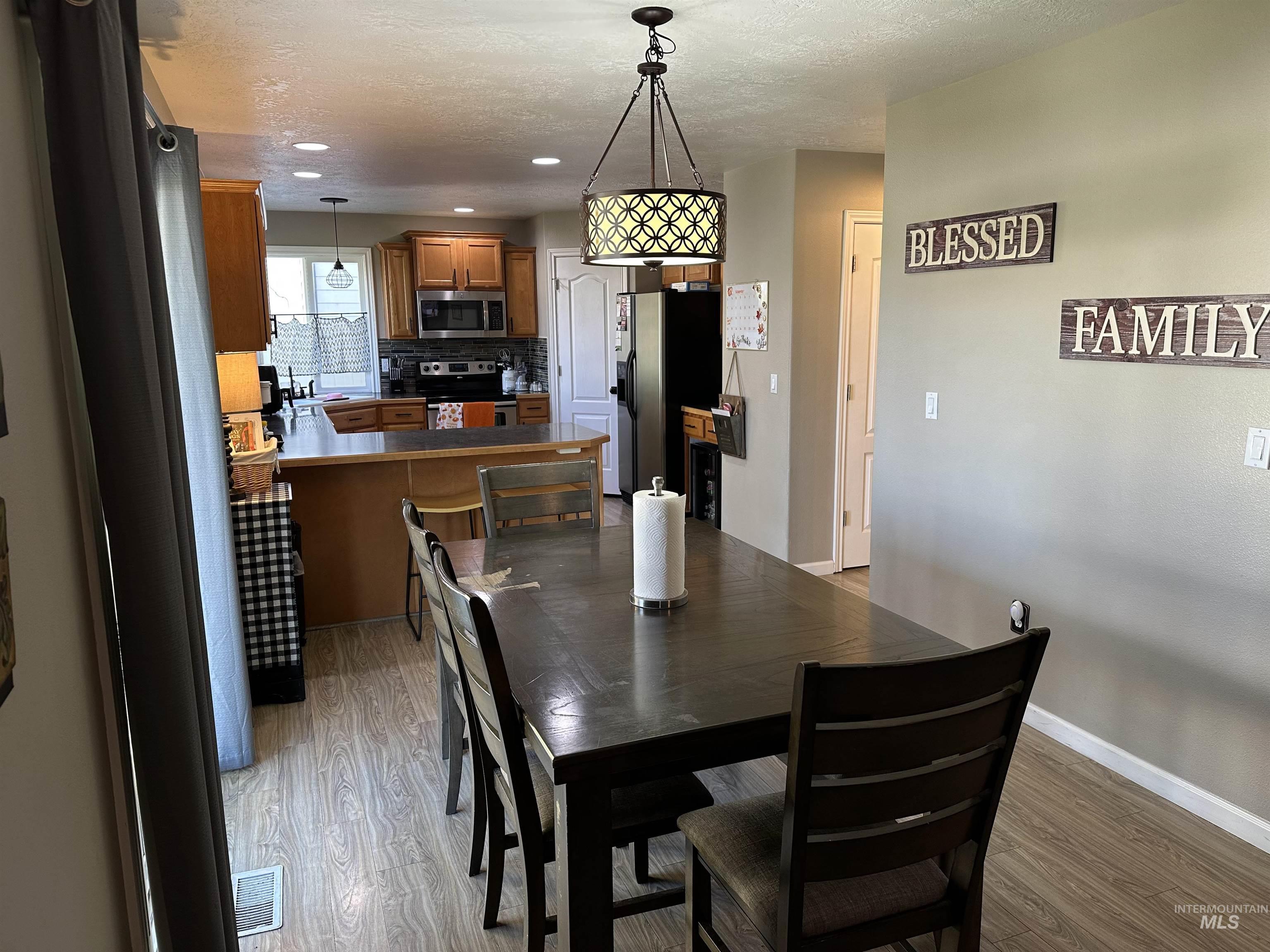 Dining room with light wood finished floors, a textured ceiling, and recessed lighting