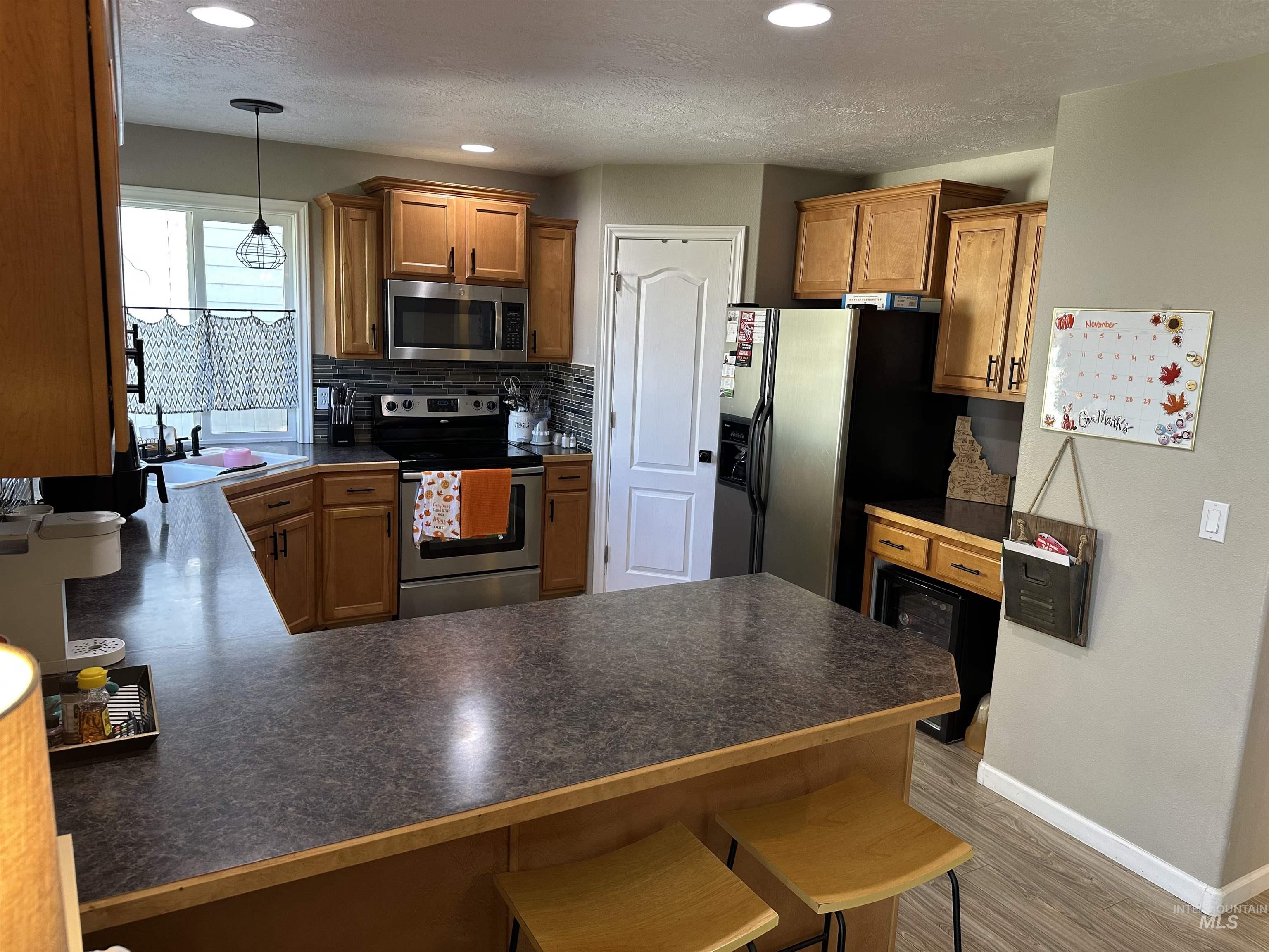 Kitchen featuring brown cabinetry, appliances with stainless steel finishes, a peninsula, dark countertops, and a textured ceiling