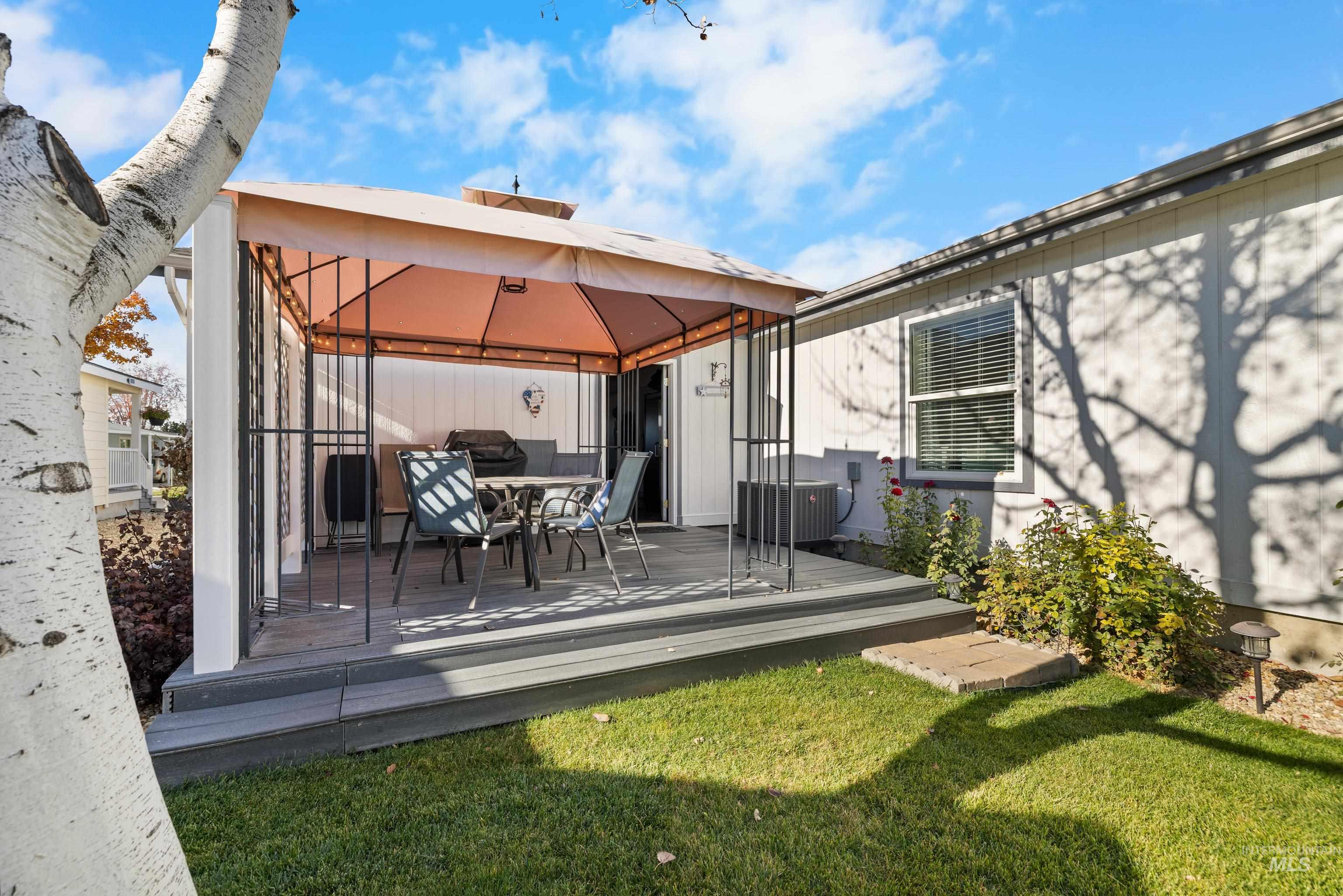 Rear view of house featuring a wooden deck, outdoor dining area, a lawn, and a gazebo