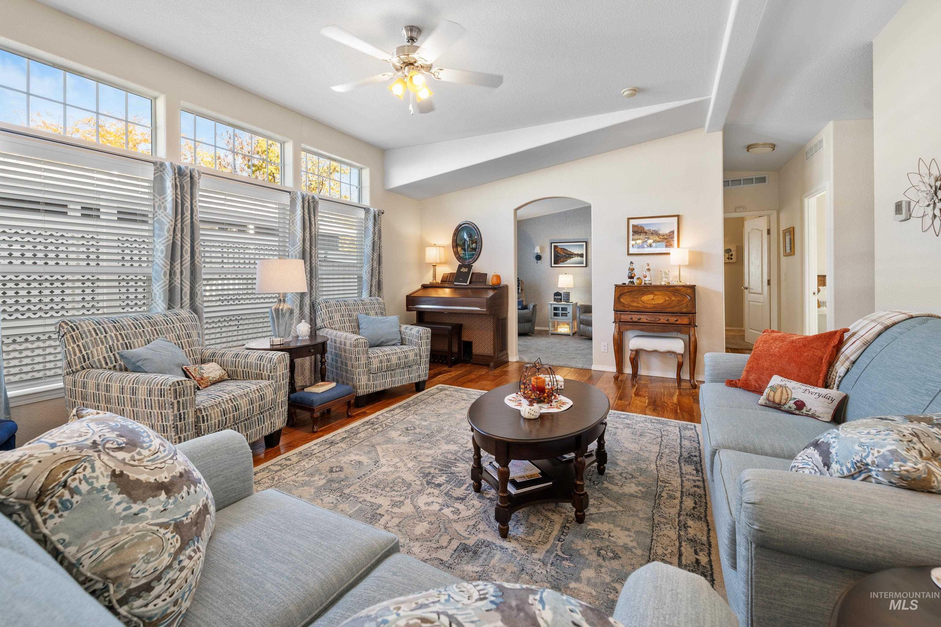 Living area with arched walkways, wood finished floors, vaulted ceiling, and a ceiling fan