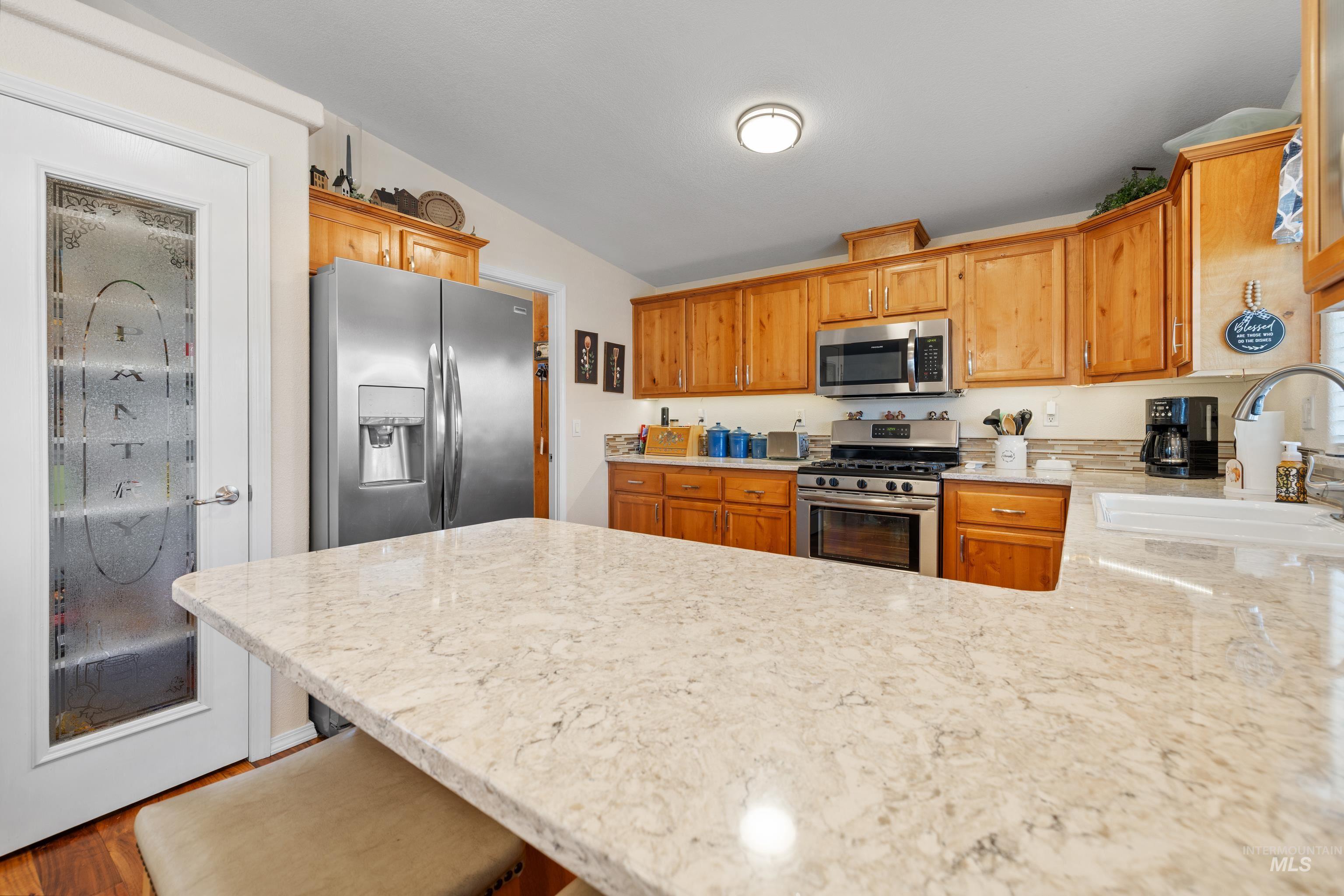 Kitchen featuring a peninsula, appliances with stainless steel finishes, light stone counters, a kitchen bar, and brown cabinets