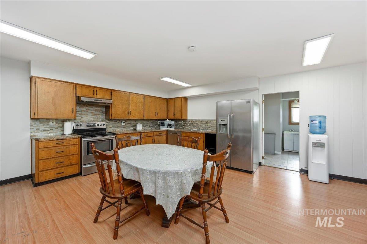 Kitchen with brown cabinets, appliances with stainless steel finishes, light wood finished floors, decorative backsplash, and under cabinet range hood