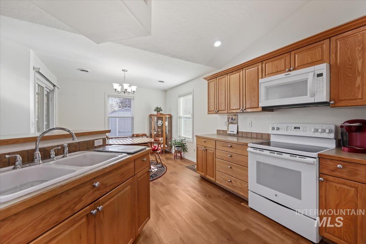 Kitchen featuring white appliances, pendant lighting, light wood-style floors, brown cabinets, and recessed lighting