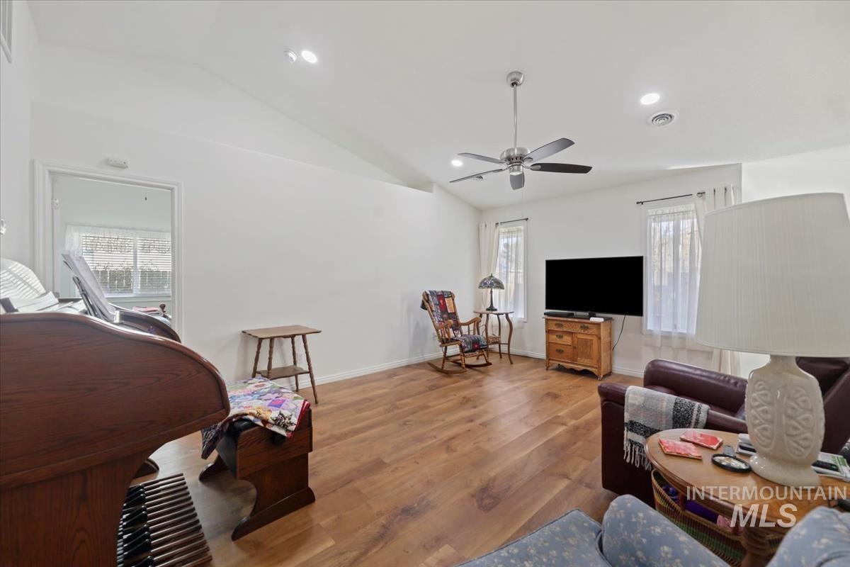 Living room with lofted ceiling, wood finished floors, a ceiling fan, and recessed lighting