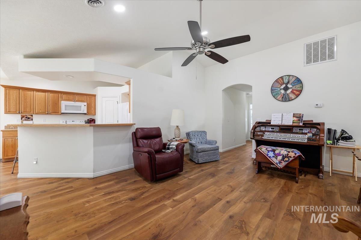 Living area with light wood-style floors, arched walkways, ceiling fan, and high vaulted ceiling