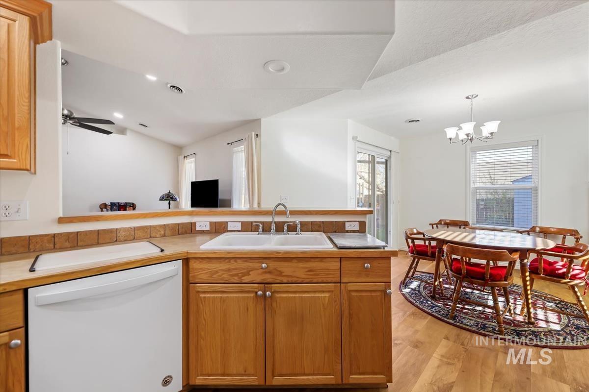 Kitchen with white dishwasher, brown cabinets, a peninsula, light wood-style flooring, and a chandelier