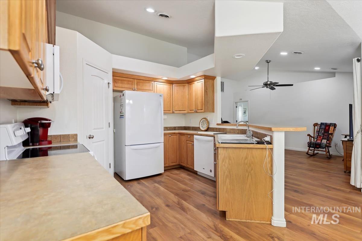 Kitchen with a peninsula, white appliances, light countertops, light wood finished floors, and recessed lighting
