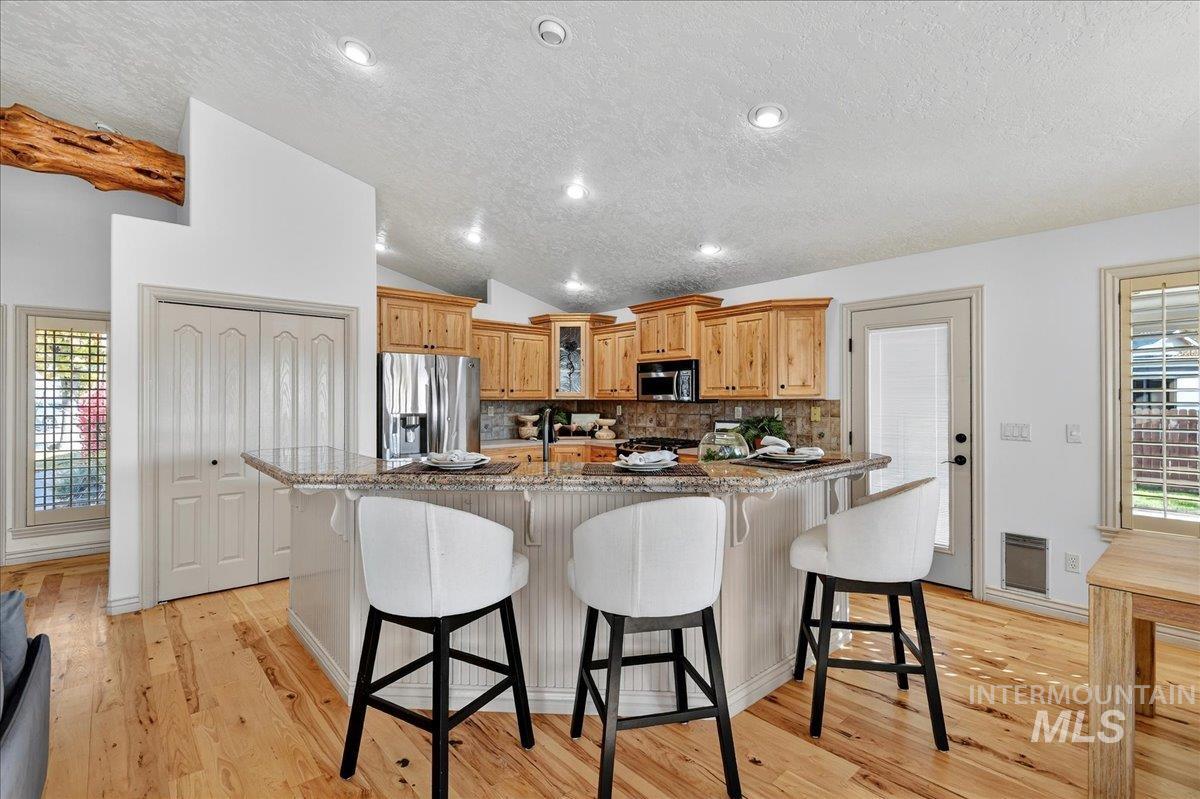 Kitchen with healthy amount of natural light, a textured ceiling, decorative backsplash, a breakfast bar, and light wood-type flooring