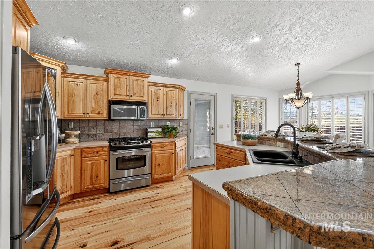 Kitchen with stainless steel appliances, tasteful backsplash, a textured ceiling, pendant lighting, and light wood-type flooring