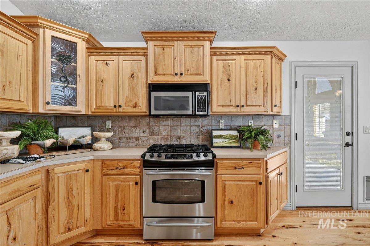 Kitchen featuring appliances with stainless steel finishes, backsplash, light countertops, a textured ceiling, and light wood-style flooring