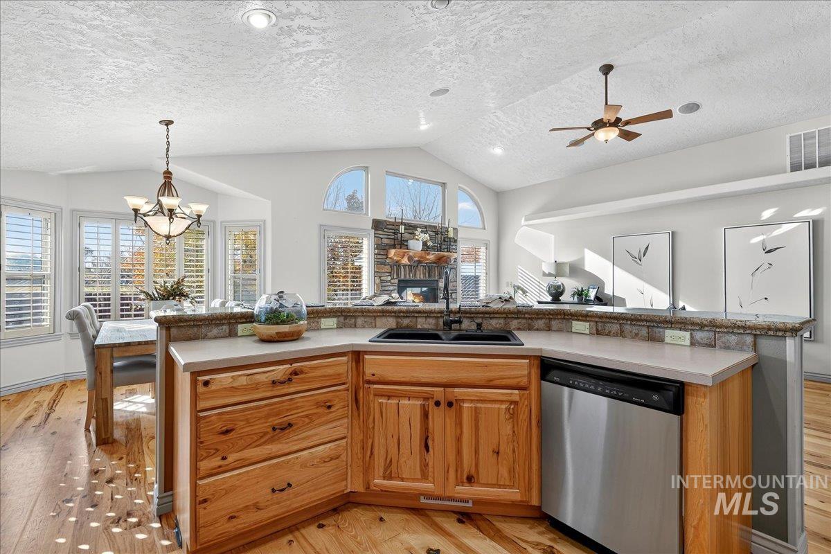 Kitchen featuring stainless steel dishwasher, light wood-type flooring, lofted ceiling, brown cabinetry, and a textured ceiling