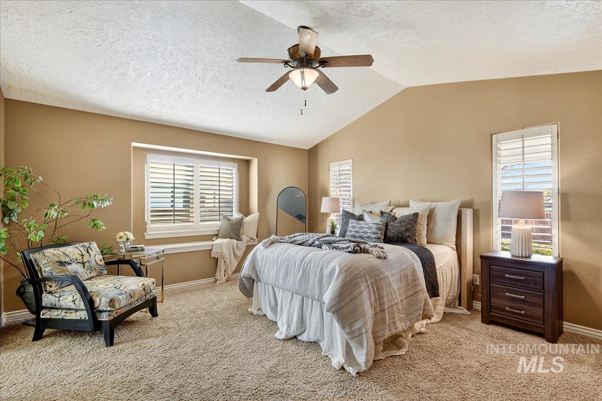 Carpeted bedroom featuring a textured ceiling, multiple windows, a ceiling fan, and lofted ceiling
