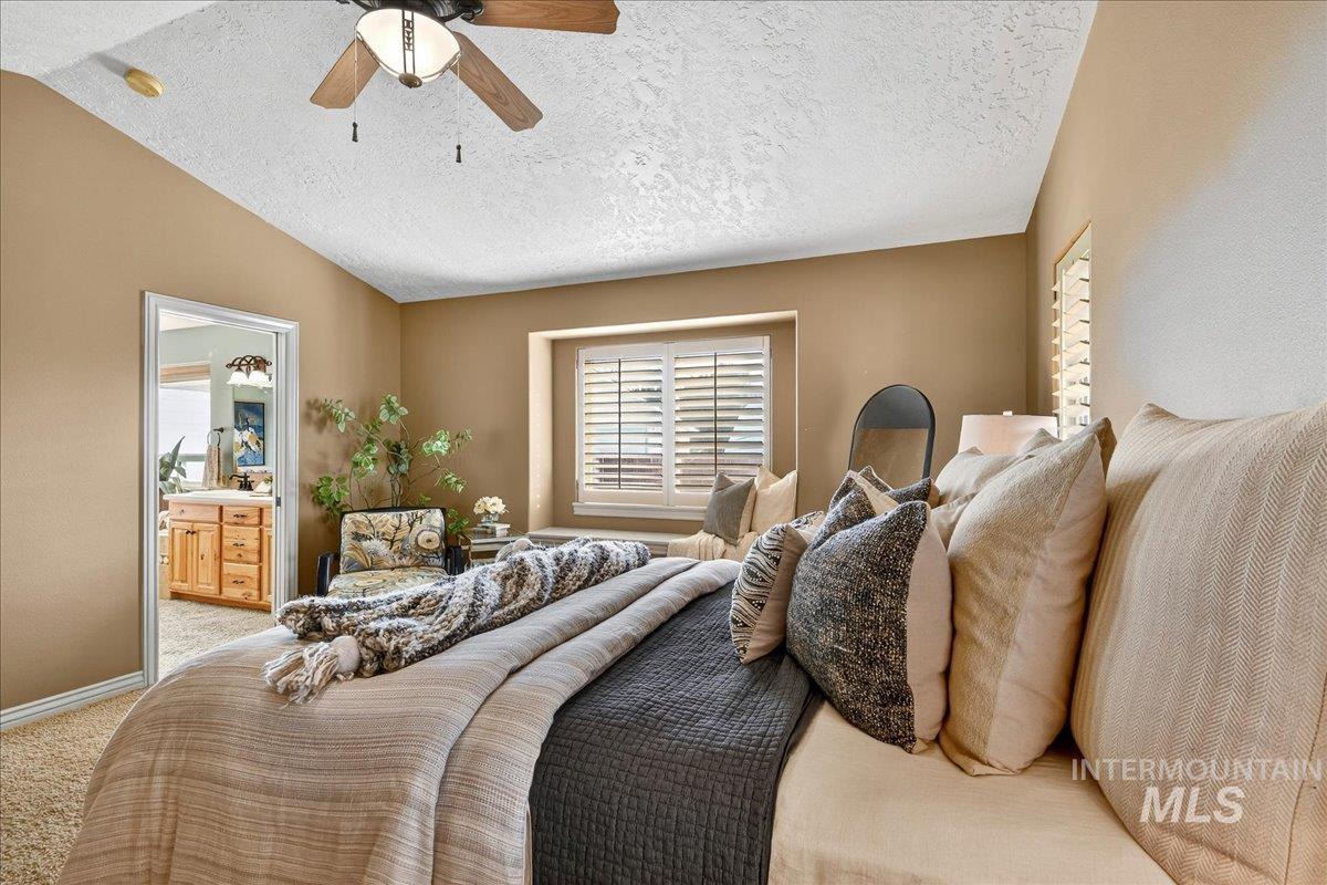 Carpeted bedroom featuring a textured ceiling, ensuite bathroom, lofted ceiling, and a ceiling fan