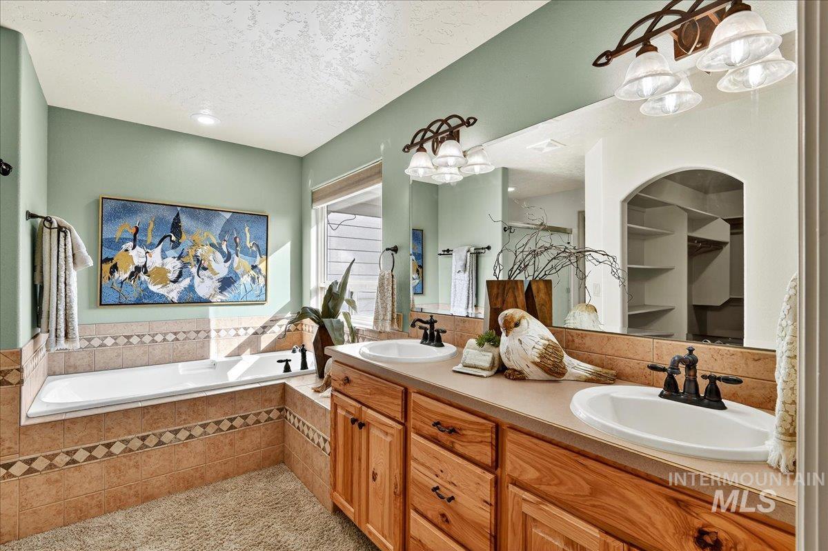 Bathroom featuring a textured ceiling, double vanity, a bath, a shower stall, and tasteful backsplash
