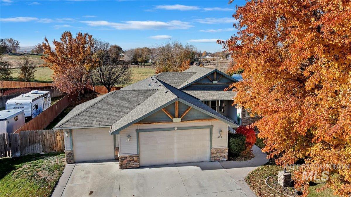 View of front facade featuring stone siding, roof with shingles, driveway, and an attached garage