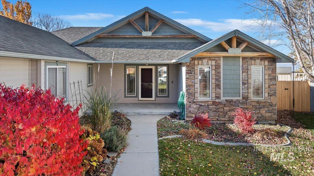 Doorway to property with covered porch, roof with shingles, and stone siding