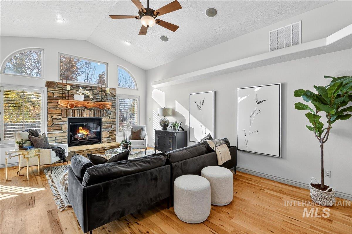 Living room with a textured ceiling, light wood-style floors, a ceiling fan, healthy amount of natural light, and a fireplace