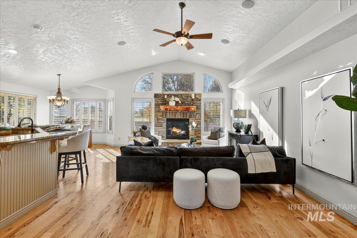 Living room featuring light wood finished floors, a fireplace, a ceiling fan, a textured ceiling, and a chandelier