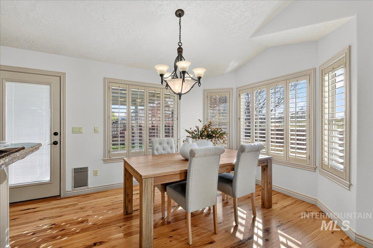 Dining space featuring a textured ceiling, light wood-style floors, a chandelier, vaulted ceiling, and heating unit