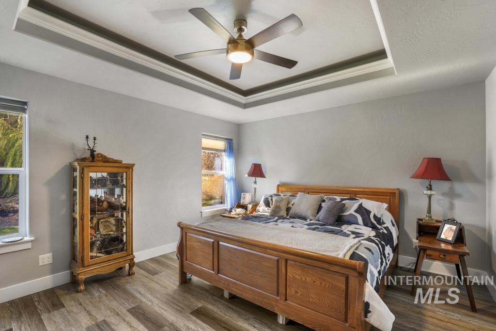 Bedroom with a tray ceiling, wood finished floors, and a ceiling fan