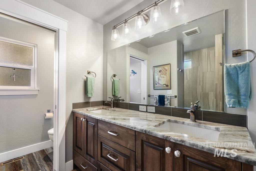 Bathroom featuring double vanity, dark wood-style floors, a tile shower, and a textured wall