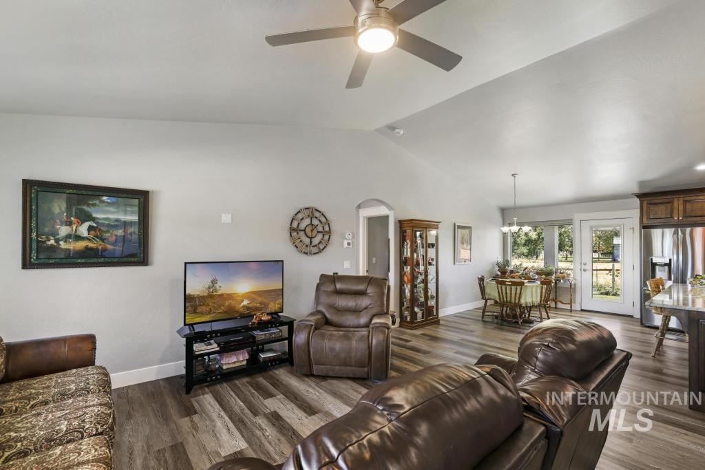 Living room with lofted ceiling, dark wood-type flooring, arched walkways, a ceiling fan, and a chandelier