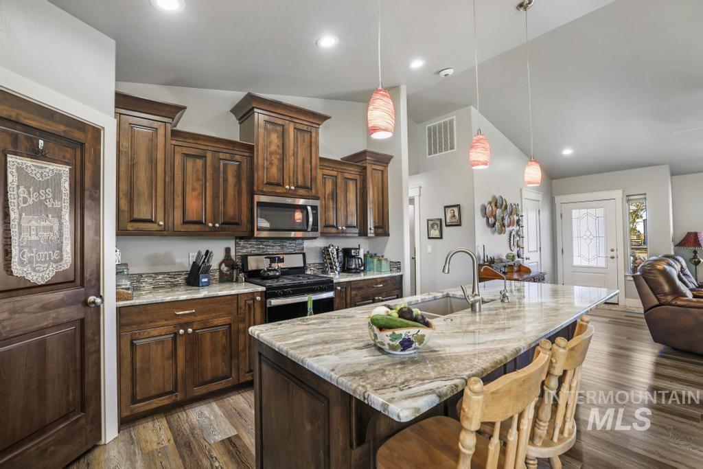 Kitchen with dark brown cabinetry, stainless steel appliances, a breakfast bar area, lofted ceiling, and light stone counters