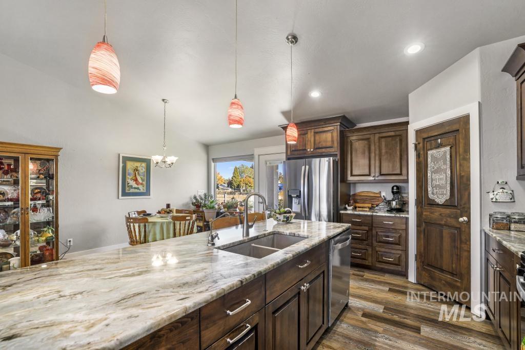 Kitchen with decorative light fixtures, dark wood-style floors, dark brown cabinetry, light stone counters, and appliances with stainless steel finishes