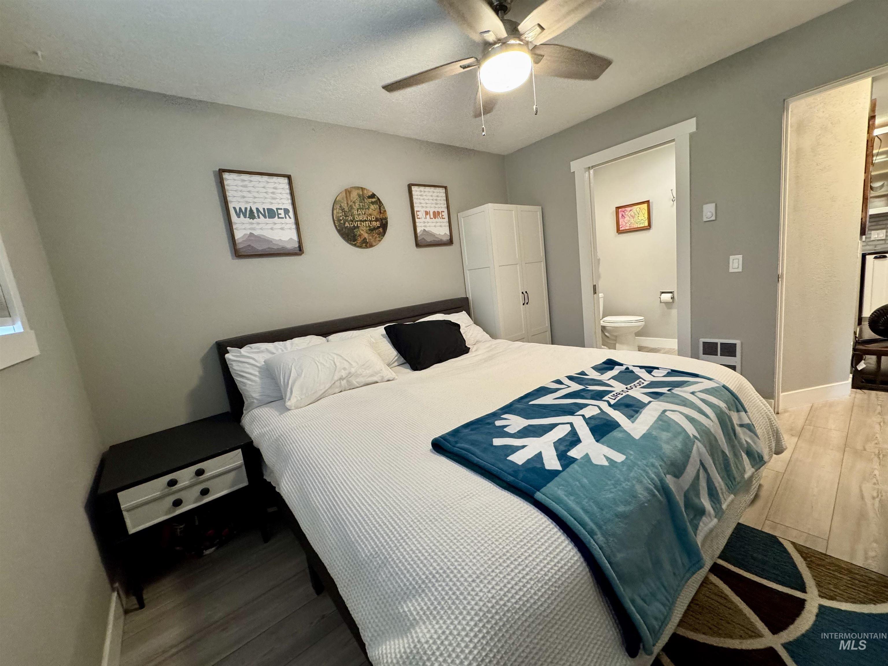 Bedroom featuring wood finished floors, connected bathroom, a ceiling fan, and a textured ceiling