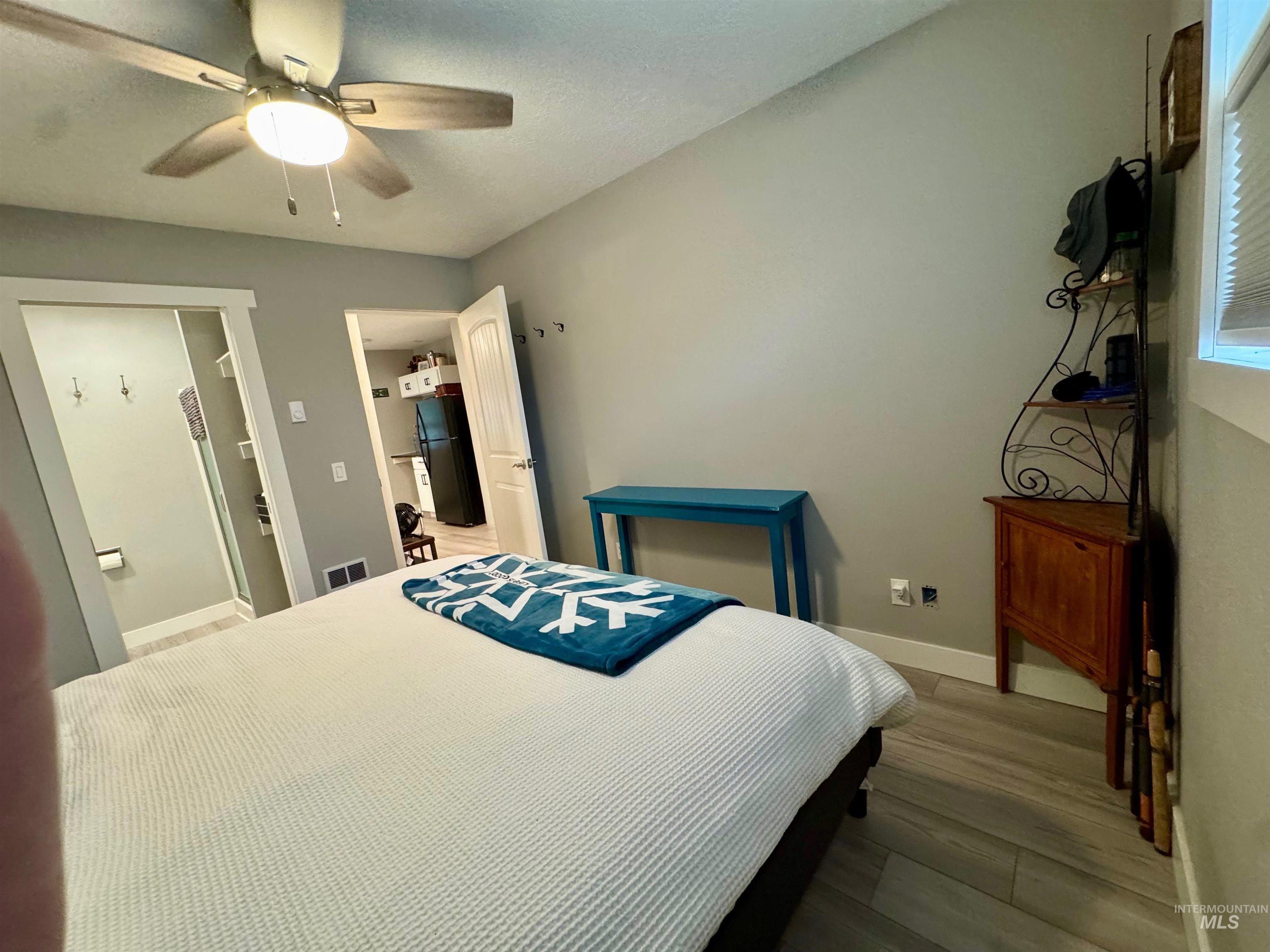 Bedroom featuring light wood finished floors, ceiling fan, and freestanding refrigerator