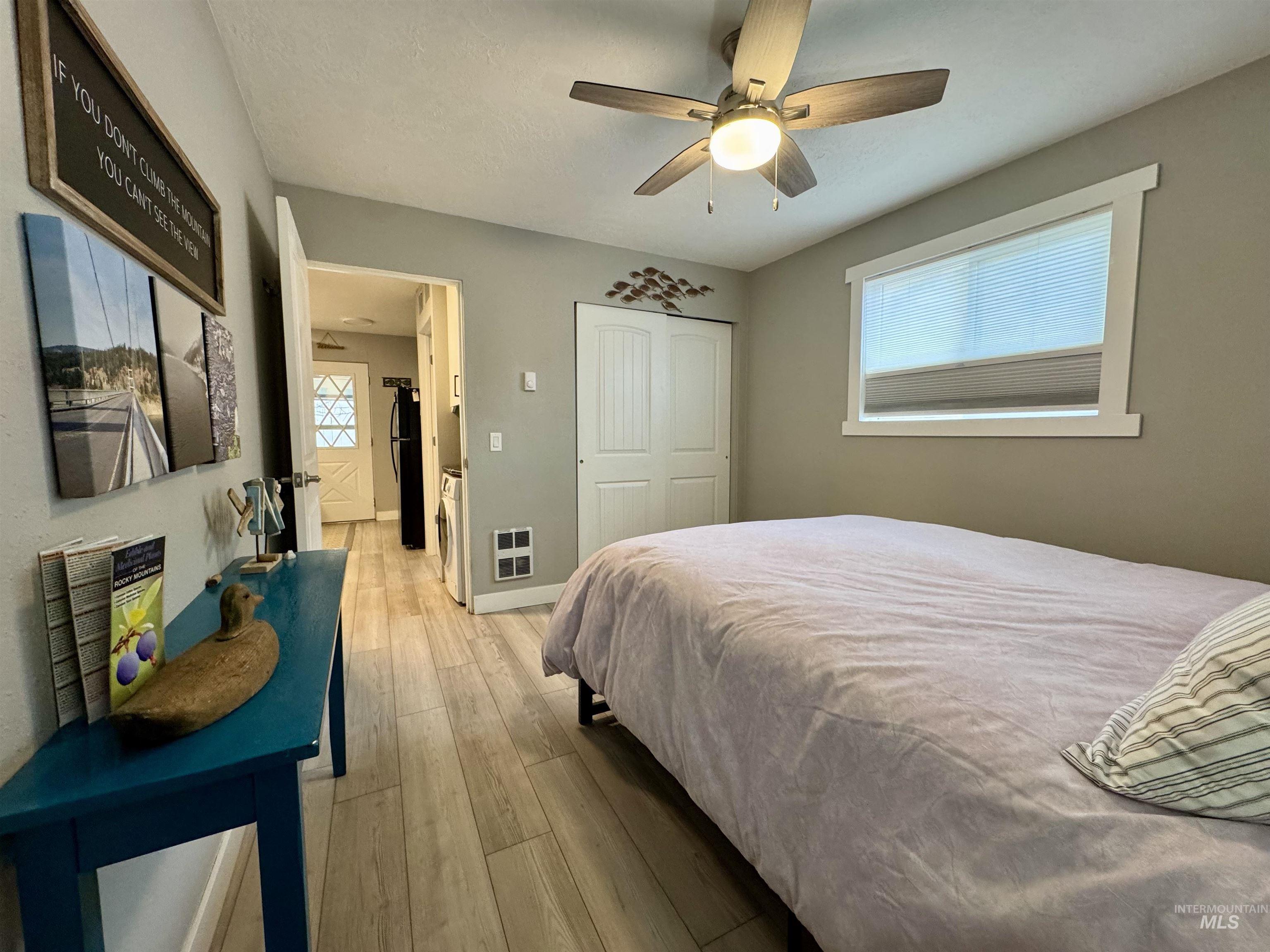 Bedroom with light wood finished floors, a closet, a ceiling fan, freestanding refrigerator, and heating unit