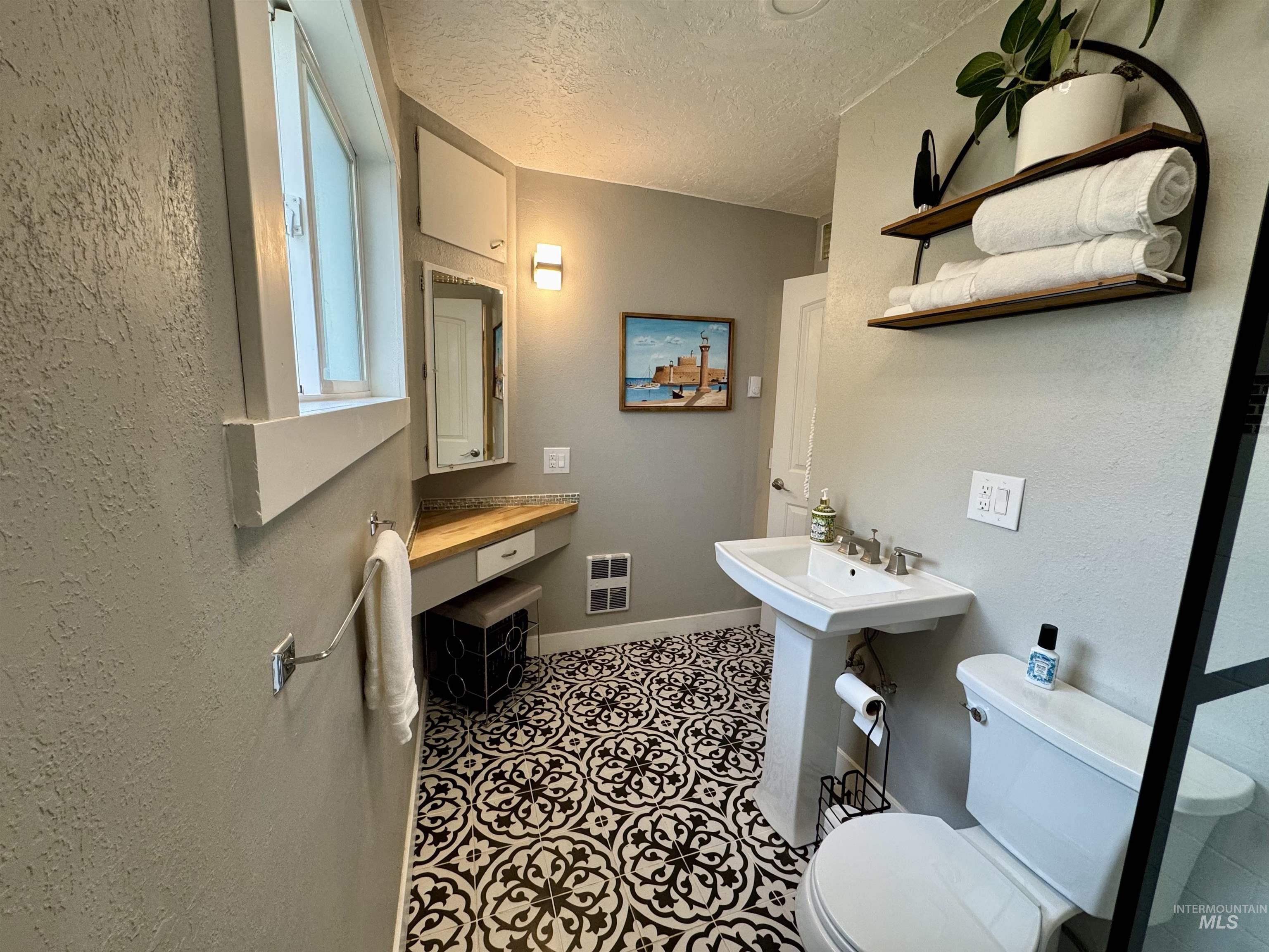 Bathroom with a textured wall, a textured ceiling, and dark tile patterned flooring