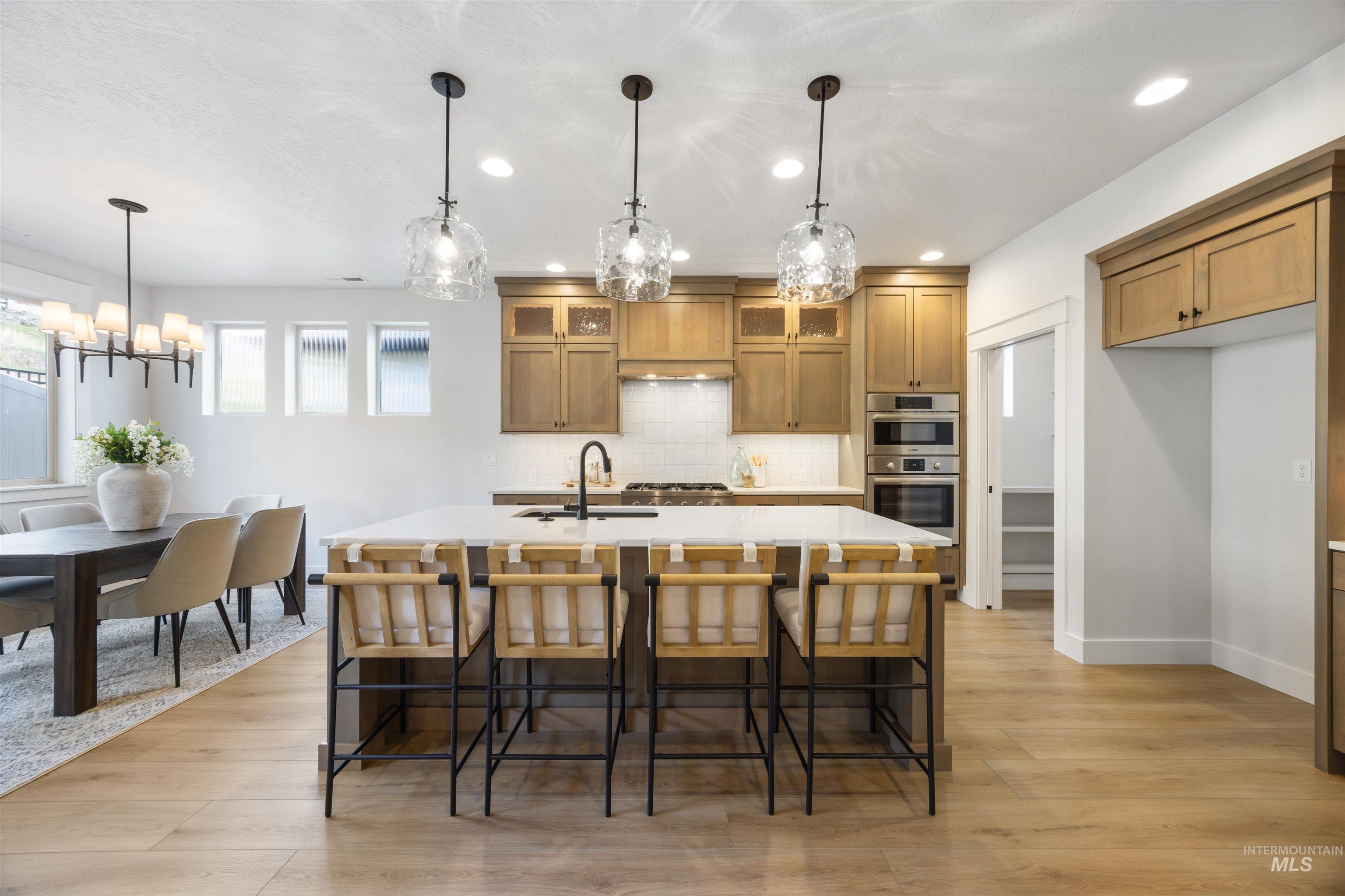 Kitchen with tasteful backsplash, pendant lighting, a kitchen island with sink, brown cabinets, and a kitchen bar