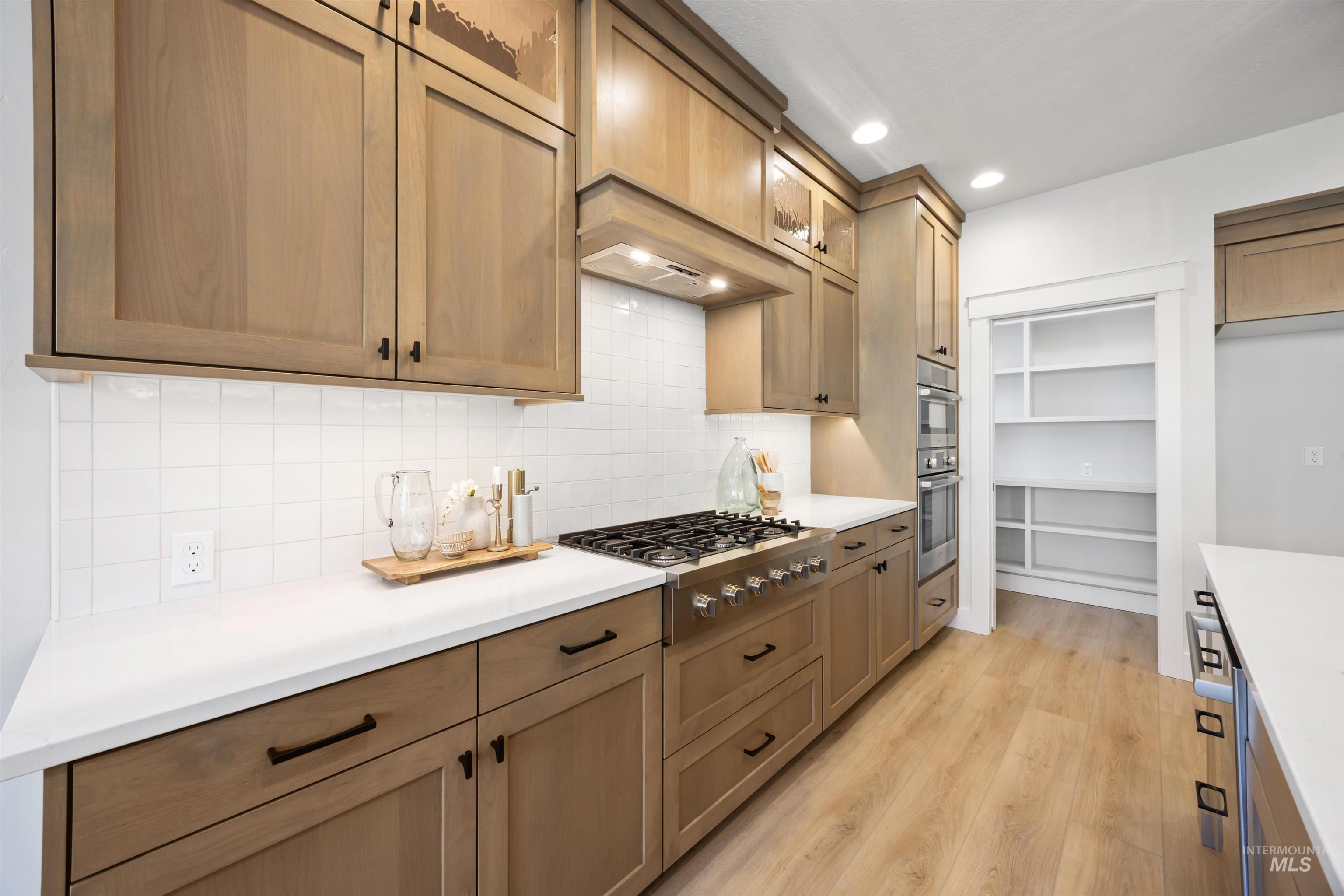 Kitchen featuring glass insert cabinets, light wood-style flooring, backsplash, stainless steel appliances, and recessed lighting