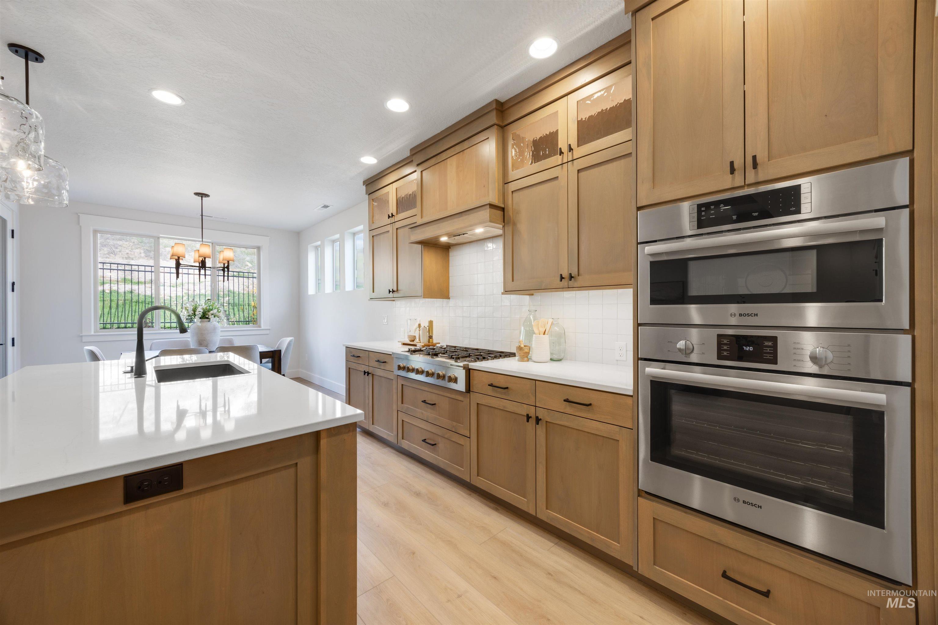 Kitchen with glass insert cabinets, stainless steel appliances, hanging light fixtures, tasteful backsplash, and light wood-type flooring