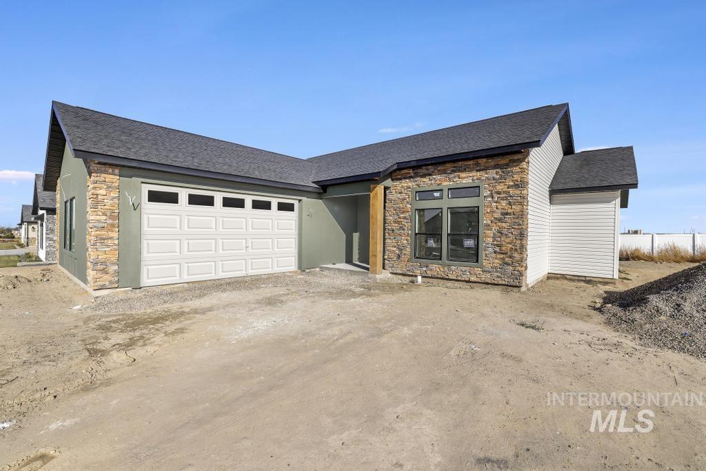 View of front of house featuring stone siding, a shingled roof, an attached garage, and driveway