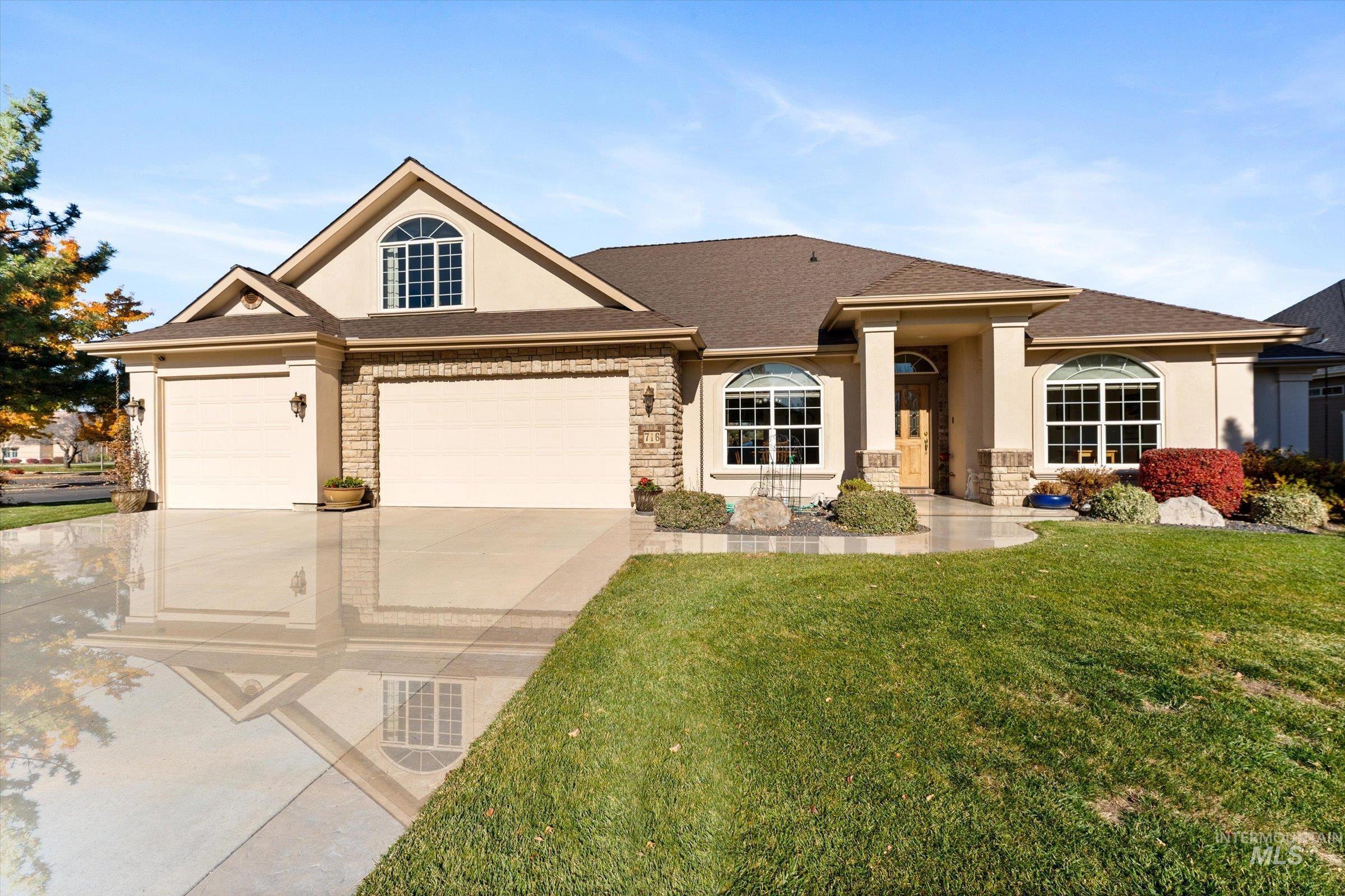 View of front facade featuring stucco siding, stone siding, a front lawn, concrete driveway, and roof with shingles