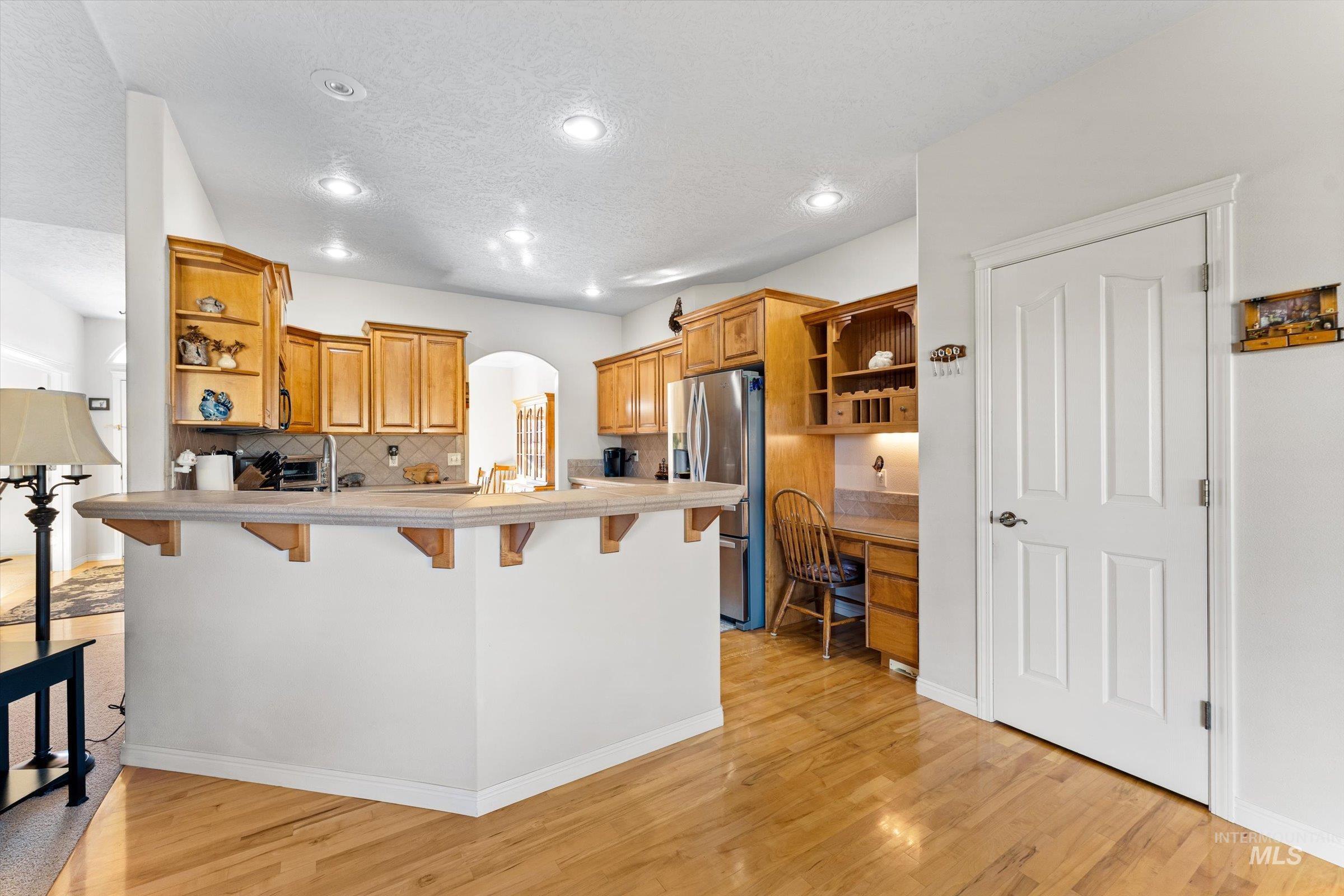 Kitchen with open shelves, arched walkways, a peninsula, a kitchen breakfast bar, and tasteful backsplash
