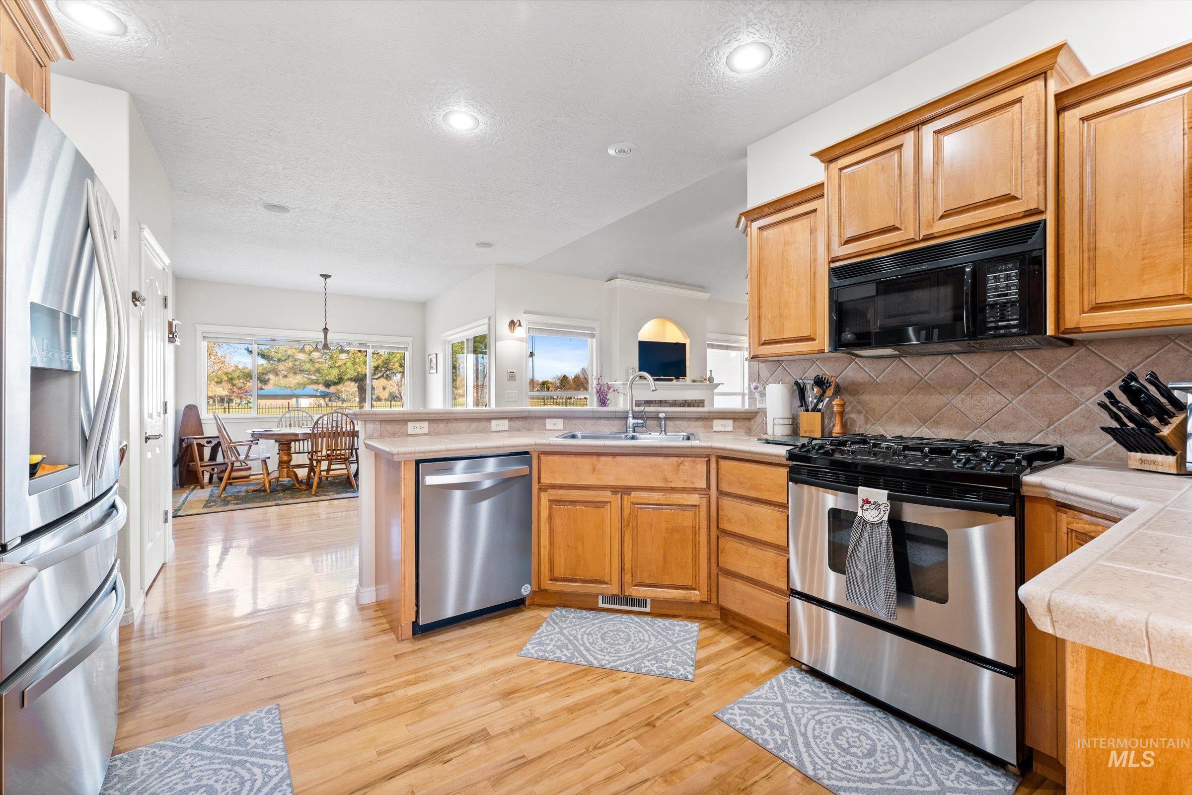 Kitchen featuring stainless steel appliances, a peninsula, backsplash, brown cabinets, and light wood-type flooring
