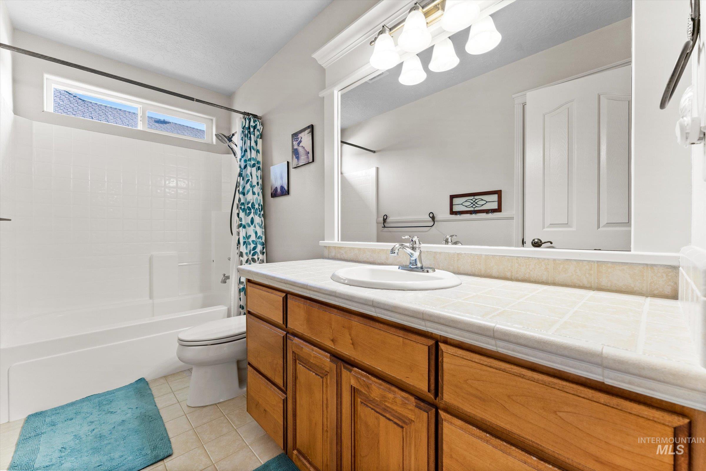 Bathroom with vanity, shower / bathtub combination with curtain, light tile patterned floors, and a textured ceiling