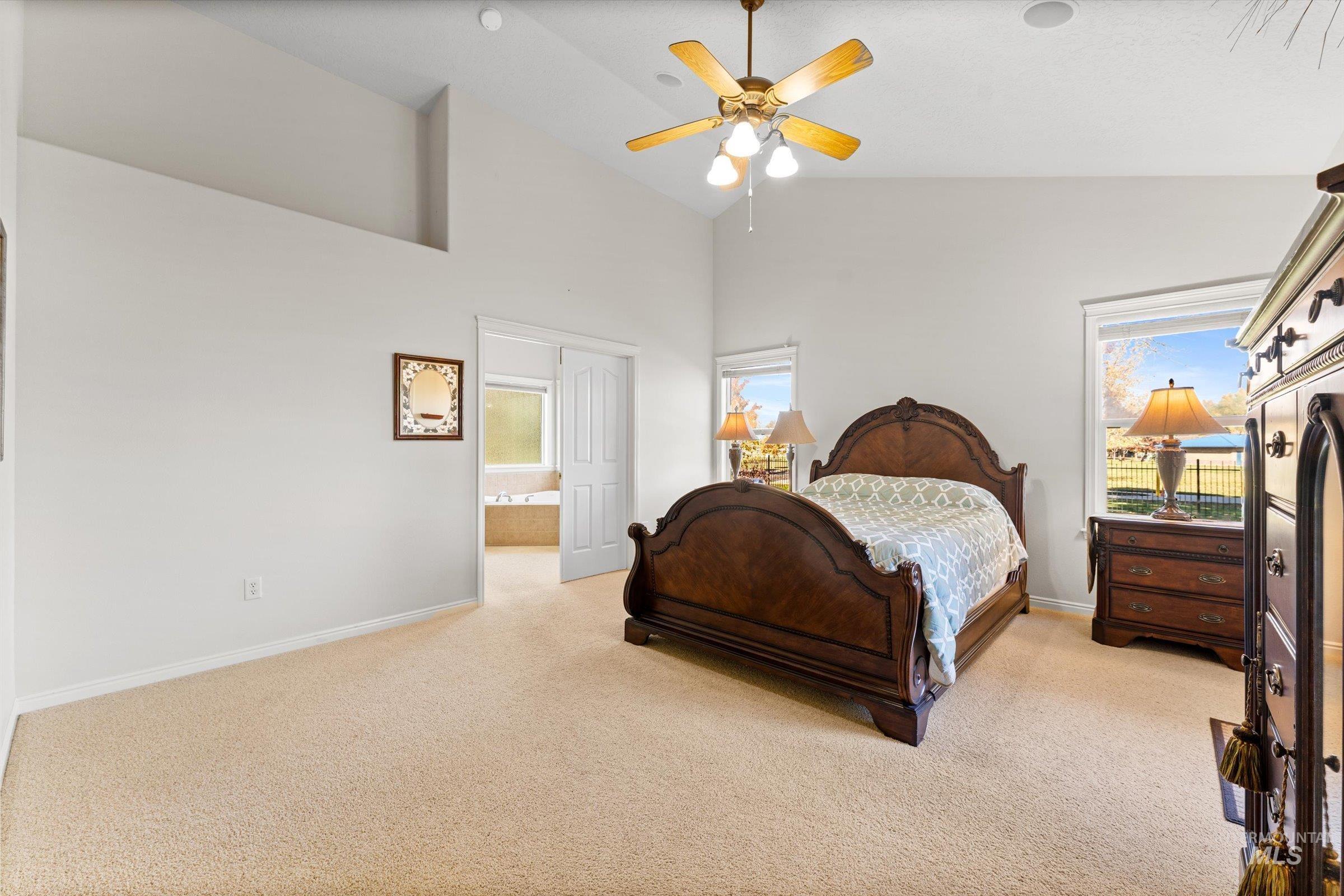 Bedroom with light colored carpet, high vaulted ceiling, a ceiling fan, and ensuite bath